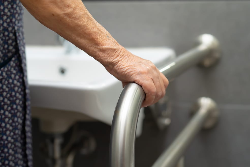 Elderly woman holding onto grab bar in bathroom for fall prevention