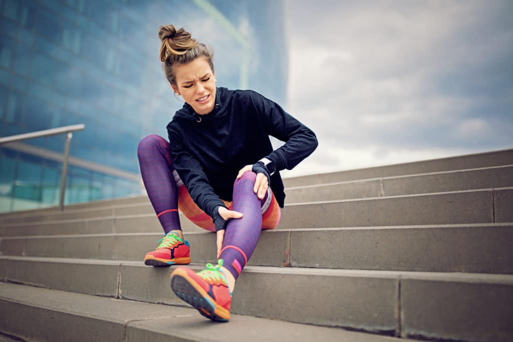 Injured runner girl is sitting on the city stairs holding her knee